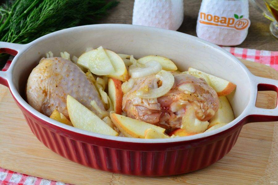 Форму для выпекания смажьте растительным маслом и выложите туда куриные голени с яблоками и луком.