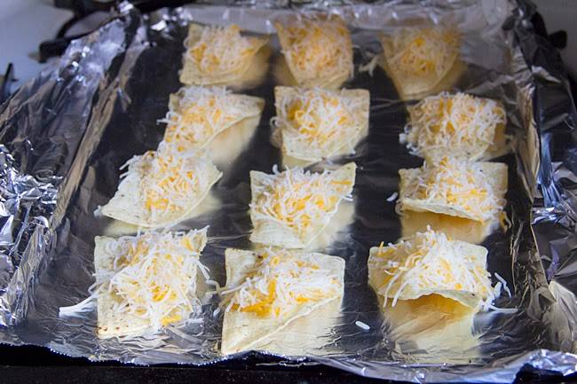 2. Тушим все вместе под крышкой, пока соус не уварится. Тем временем чипсы раскладываем на противень, застеленный фольгой. На каждый кусочек помещаем ложку-другую тертого сыра.
