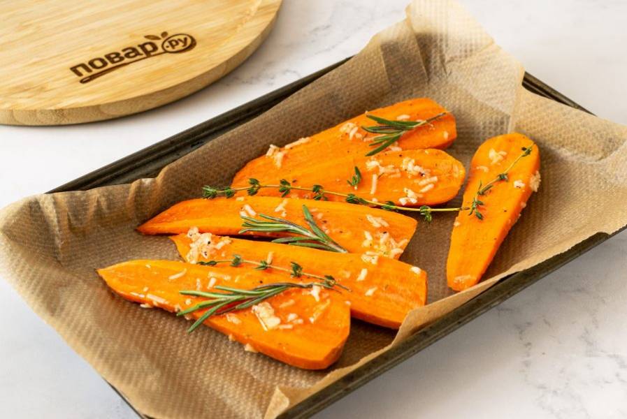 Выложите морковь на противень. Добавьте веточки розмарина и тимьяна. Запекайте в разогретой до 185 градусов духовке 35-45 минут.