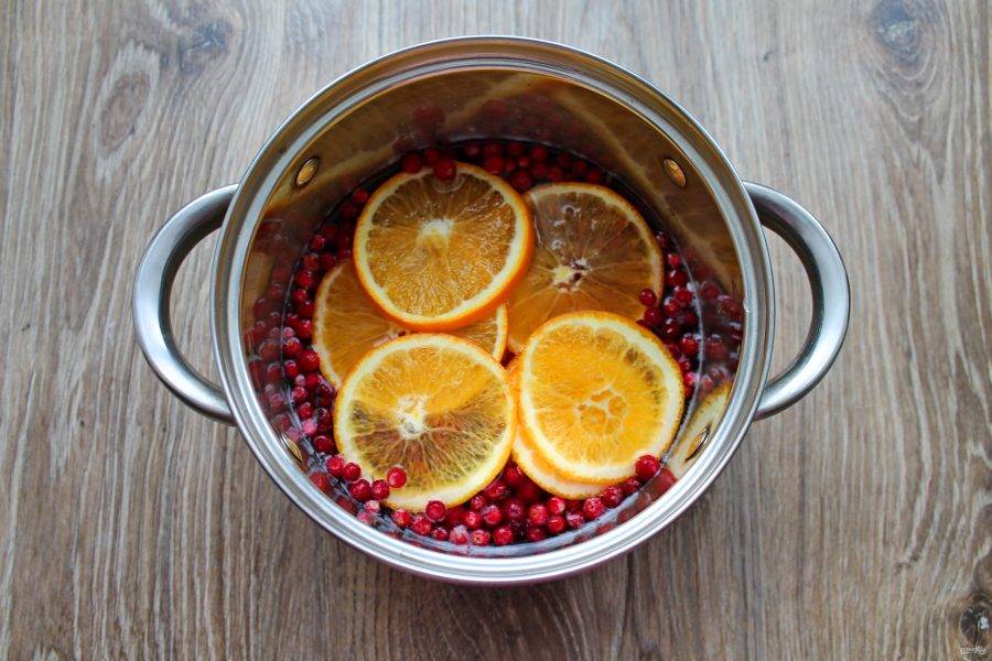 Апельсин нарежьте колесиками и выложите в кастрюлю с ягодами и лимоном.