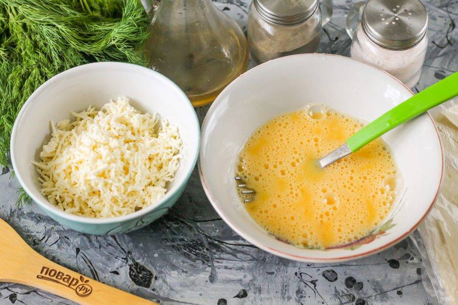 Брынзу попробуйте на вкус, натрите на терке в пиалу или глубокую тарелку. Если сыр не соленый, то чуть присолите его. Куриные яйца вбейте в миску, посолите и взбейте в течение 1-2 минут.