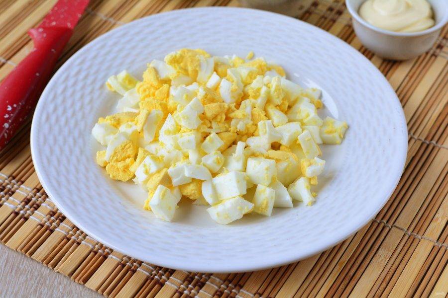 Заранее отварите куриные яйца вкрутую, затем остудите их и почистите. Нарежьте яйца кубиками для салата.