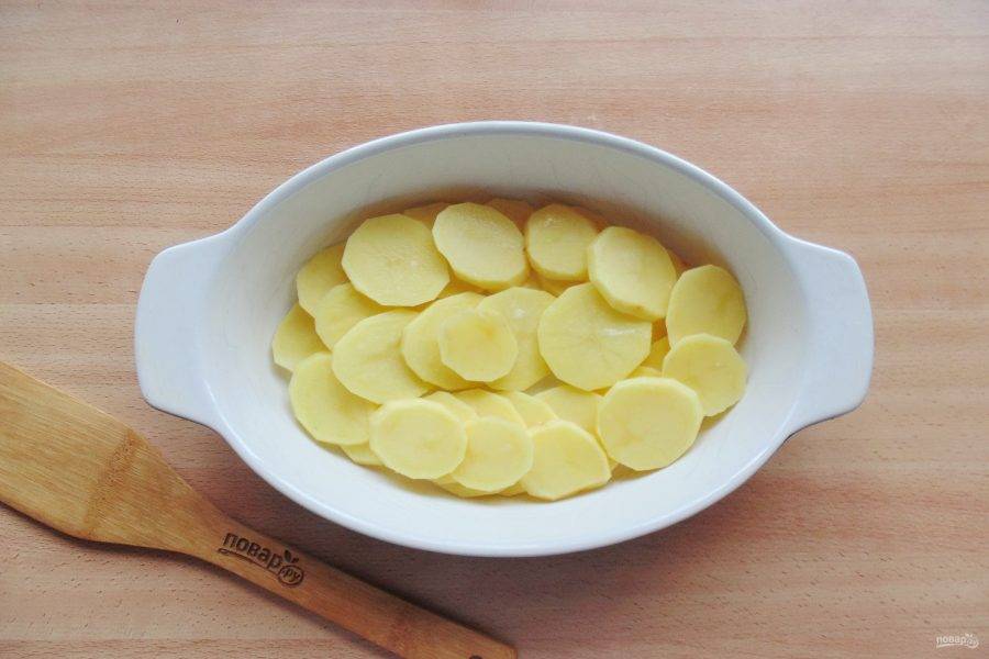 Картофель очистите, помойте и нарежьте тонкими пластинами. Выложите в форму смазанную маслом. Посолите немного.