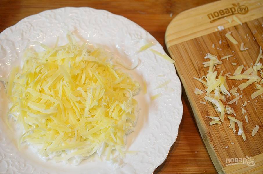 Следующим слоем выложите натертый сыр и чуть-чуть майонеза.