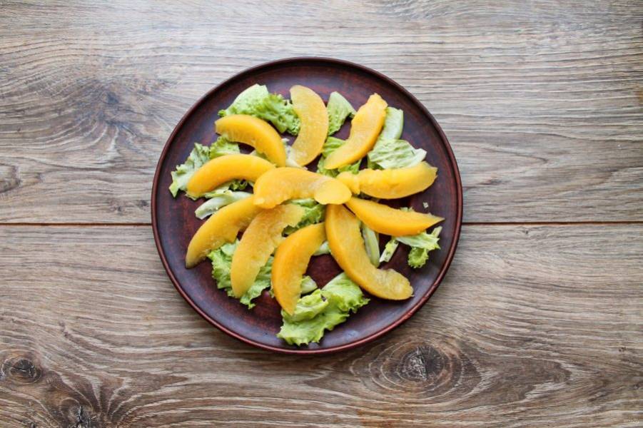 Персик порежьте на тонкие дольки и разложите поверх салатных листьев.