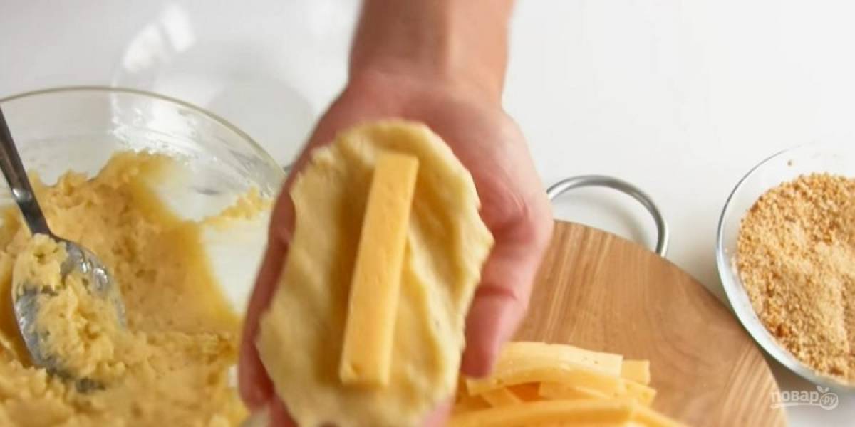 2. Тесто получится липким. Сыр нарежьте брусочками. Влажными руками сформируйте лепешку из теста, посредине выложите сыр и защипните края лепешки. Обваляйте палочки в панировочных сухарях. 