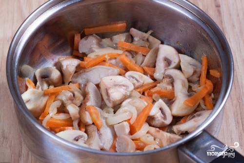 В кастрюле растопите сливочное масло. Поджарьте на нём лук до мягкости, а потом добавьте морковь. Готовьте до румяного цвета. Затем добавьте грибы и держите на небольшом огне ещё 6 минут.
