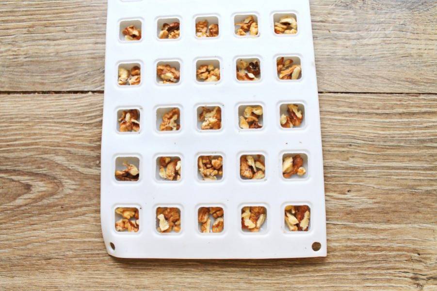 Ядра орехов освободите от скорлупы и разложите по ячейкам формы для конфет.