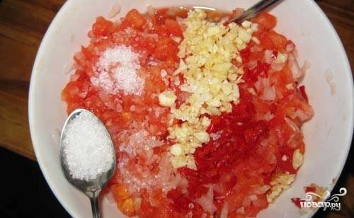 Очистите перец чили от маленьких белых семечек, после чего мелко нарежьте его. Чеснок подавите плоской стороной ножа и также нарежьте. Добавьте его к томатам с луком, посолите. Я добавляю 2 ложки соли без горки.