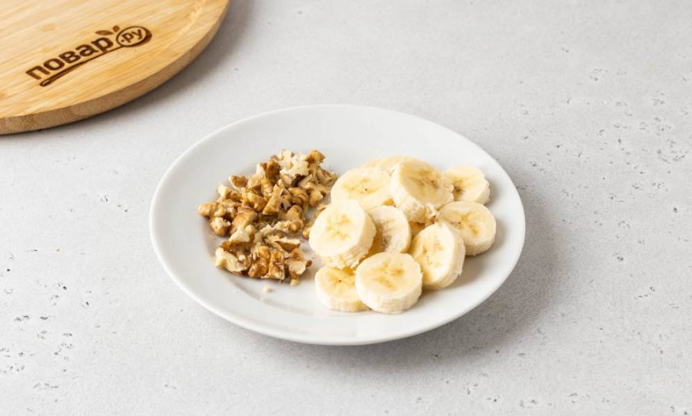 Орехи подсушите в сковороде и крупно порубите. Банан очистите и нарежьте кружочками.