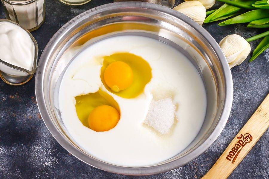 В глубокую емкость влейте кефир любой жирности, вбейте куриные яйца, всыпьте соль и 4 ст.л. сахарного песка. Взбейте в течение 1 минуты.