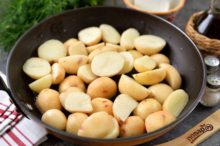 Разогрейте в сковороде растительное масло, выложите в него разрезанный пополам молодой картофель, жарьте на умеренном огне минут 15. 