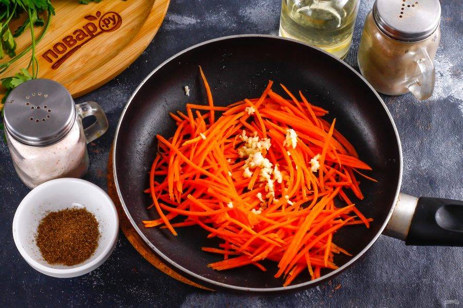 Морковь очистите от кожуры и промойте в воде. Натрите на терке для моркови по-корейски и выложите нарезку на сковороду, влив туда же 1 ст.л. растительного масла. Спрессуйте очищенный зубчик чеснока.