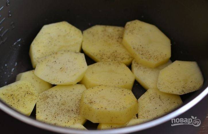 Картофель вымойте и очистите от кожуры. Затем нарежьте его на кружочки толщиной около 0,5 см. Выложите картошку на дно чаши мультиварки, приправьте солью и перцем. 