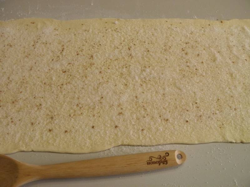 2. Размороженное тесто разложите на присыпанном мукой столе. Разровняйте его. Посыпьте щедро сахаром и корицей, скалкой вкатайте сахар в тесто.