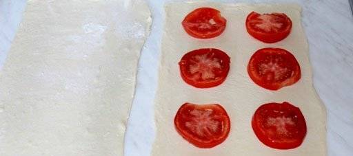 Тесто раскатайте в две полосы. На одну часть выложите кружочки помидоров.