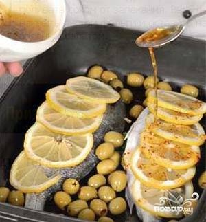 Противень смазываем маслом, выкладываем на него рыбу. Кружочки лимона споласкиваем и выкладываем на рыбу. Засыпаем поверху оливки и поливаем смесью оливкового масла и специй.