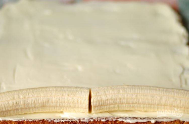 Выложите начинку на бисквит и равномерно, при помощи лопатки, распределите ее по поверхности. Очистите два банана и выложите их на начинку с одной стороны. 