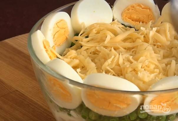 6. В центр поместите слой тертого сыра с сеточкой из майонеза. Накройте это тертыми яйцами и украсьте горошком. 