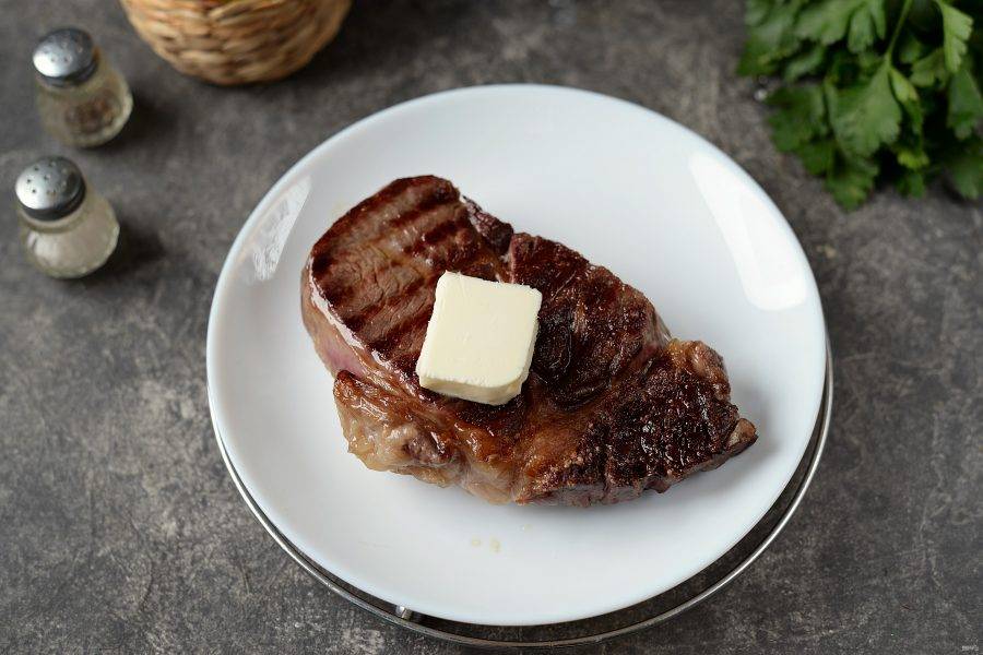 Переложите стейк на теплую тарелку, которую можно быстро нагреть в микроволновке. Смажьте мясо со всех сторон кусочком сливочного масла. 