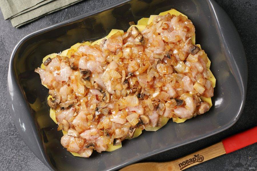 Соедините кусочки куриного филе и обжаренные грибы с луком. Выложите равномерно на картофель.
