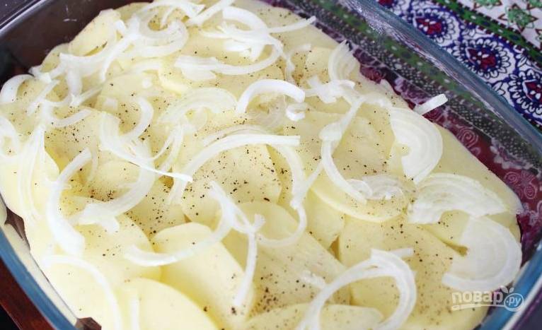 Разогрейте духовку до 180 градусов, картофель нарежьте тонкими кружками и выложите первый слой картошки в форму. Сверху выложите порезанный тонкими полукольцами лук, присыпьте солью и перцем.