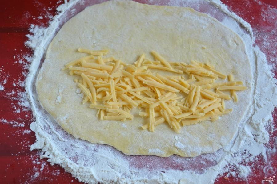 Тесто разделите на 4-5 частей (в зависимости от того, какие чебуреки по размеру вы хотите получить). Раскатайте каждую часть в форме круга, условно поделите круг пополам, на одну половину положите тертый сыр.