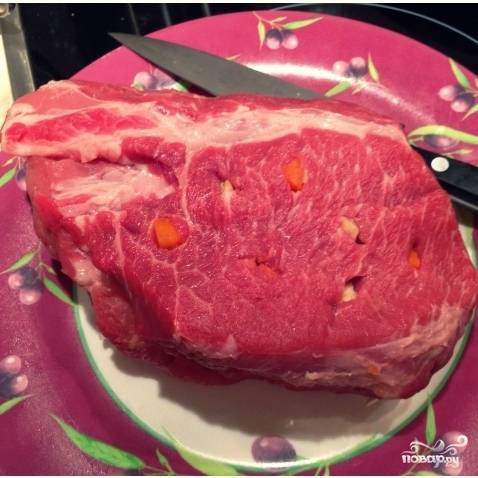 Мясо нашпигуйте морковью и чесноком. Для этого проткните мясо острым длинным ножом в разных местах, а затем засуньте кусочки овощей в надрезы. Следите за тем, чтобы со всех сторон мясо было равномерно нашпиговано.