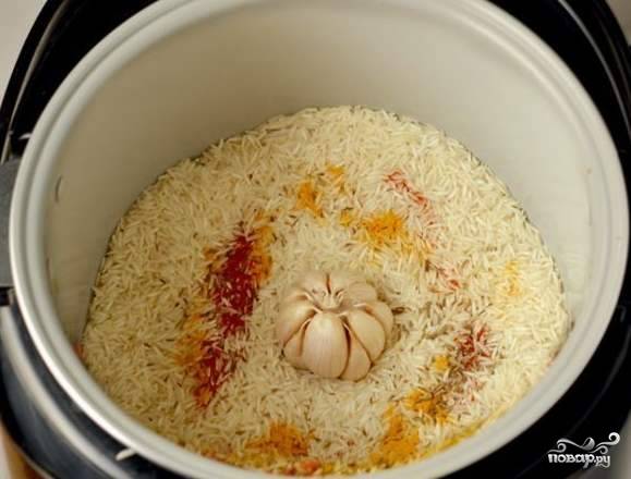 Рис тщательно промываем и высыпаем на мясо с овощами. Помещаем в центр головку чеснока, очищенную от верхней шелухи, добавляем специи и соль.