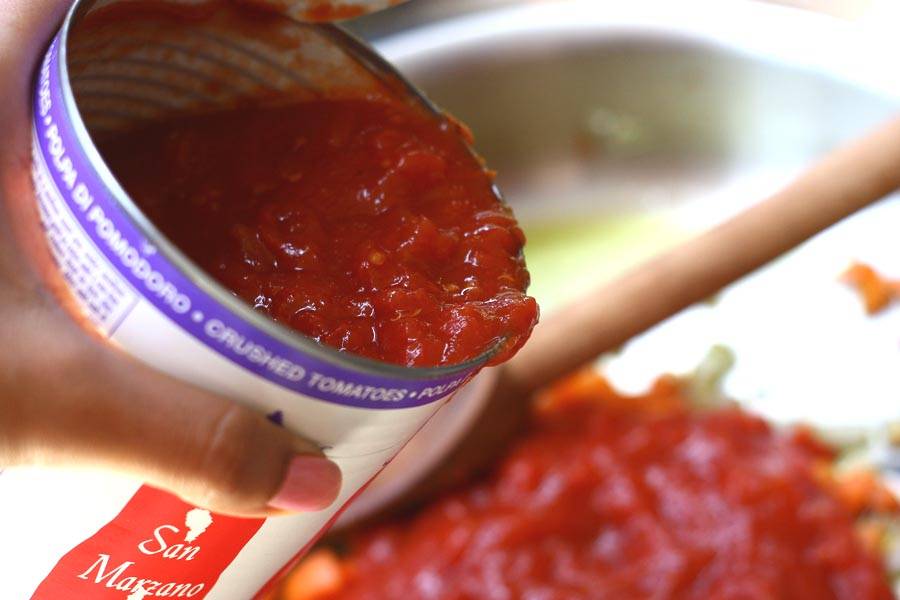 4. Затем в сковороду выложите консервированные помидоры с соком. Если они - целые, предварительно измельчите. Добавьте в сковороду. 