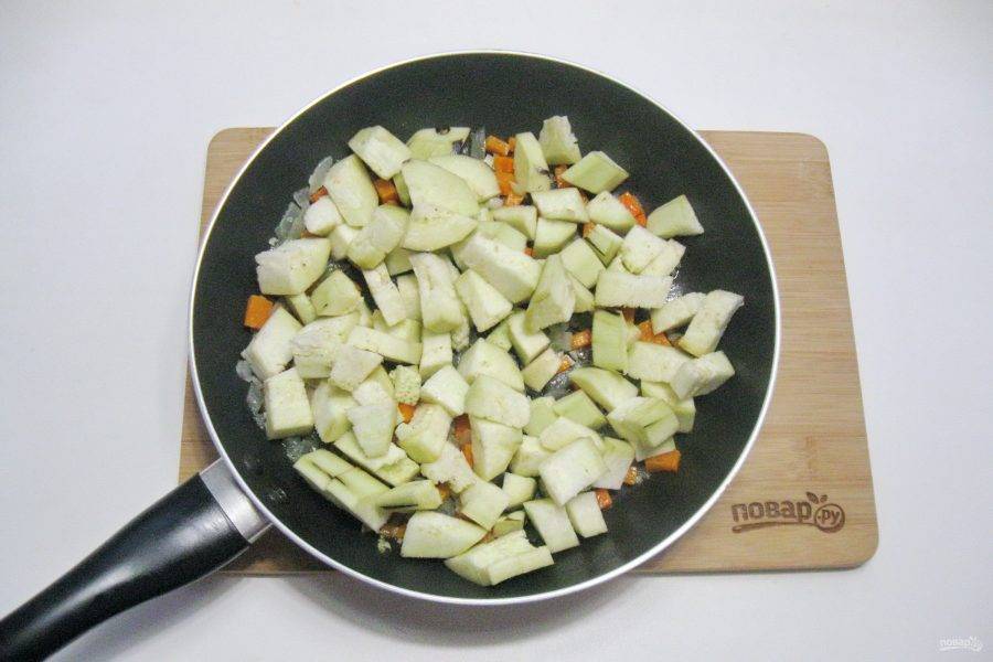 Один крупный баклажан помойте, очистите и нарежьте кубиками. Выложите в сковороду с овощами. Налейте 50 мл. воды, накройте сковороду крышкой и тушите овощи с баклажаном 7-8 минут.