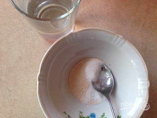 В небольшой глубокой миске смешаем сухие дрожжи и сахар, добавим стакан теплой воды. Размешаем и поставим в теплое место.