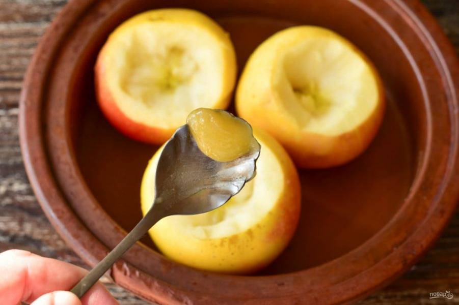 Выложите по половинке чайной ложки меда в каждое яблоко.