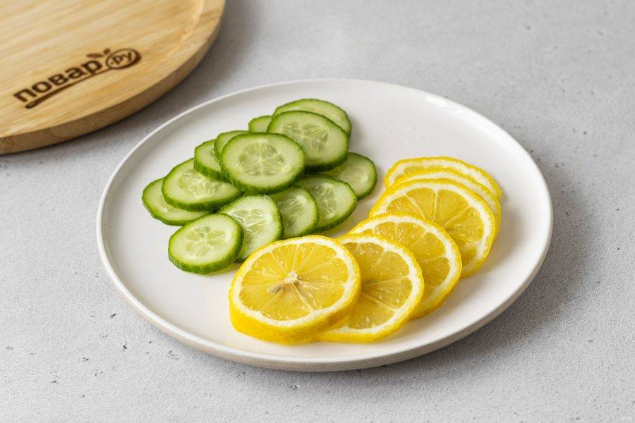 Помойте лимон и огурец. Нарежьте тонкими кружочками.