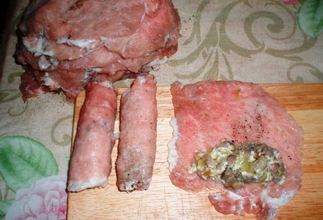 Берем один кусочек отбитого мяса и выкладываем на его край немного начинки, скручиваем в рулетик. То же самое повторяем с остальными кусочками мяса.