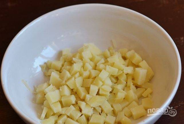 Картофель вымойте и поместите в кастрюлю. Залейте его водой и отварите до готовности. Остудите картофель, очистите его от кожуры. Нарежьте кубиками и выложите в миску. 