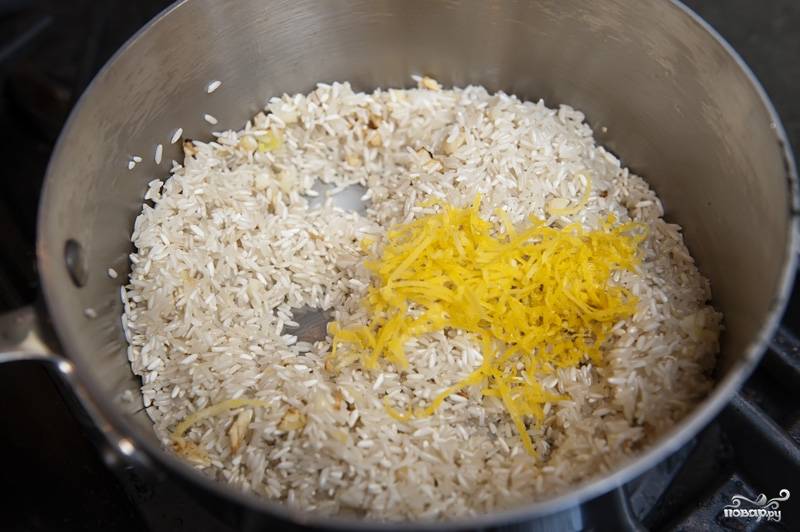 В кастрюльке среднего размера разогреваем оливковое масло. Добавляем чеснок и рис, хорошенько все размешиваем в течении нескольких минут, пока рис не начнет белеть. Добавляем цедру лимона.