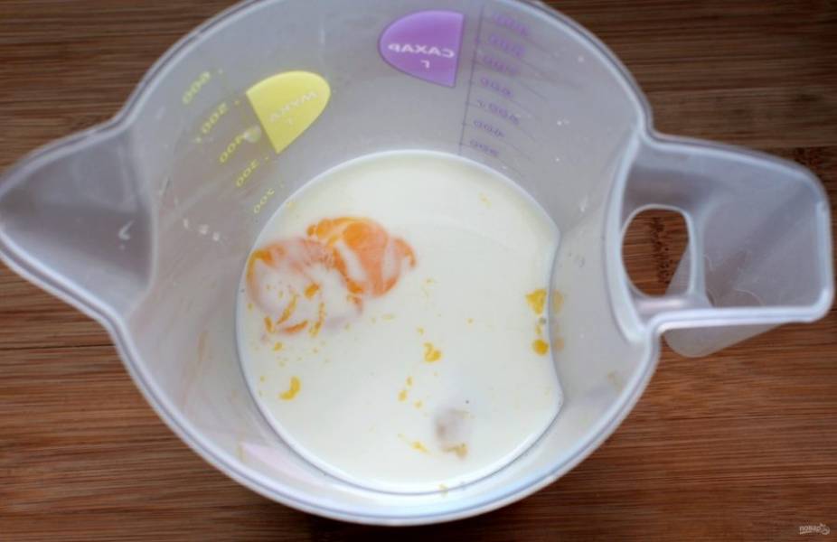  Отмеряйте теплое молоко и вбейте в него яйцо и два желтка. Взбейте венчиком и вылейте в муку.