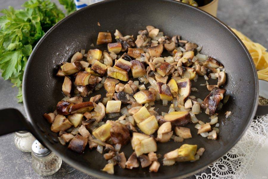 Разогрейте в сковороде оливковое масло, положите в него нарезанный лук, шампиньоны и белые грибы. Жарьте на умеренном огне минут 7-10.