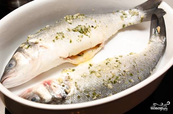 Жаропрочную посуду смажьте оливковым маслом, чтобы продукты не прилипали к нему в процессе запекания. Выложите на блюдо подготовленную рыбу. Обильно смажьте сибаса чесночным маринадом. 