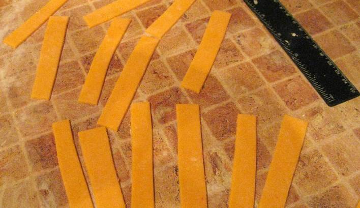 Теперь займемся бантом. Из оранжевой мастики раскатываем пласт и нарезаем одинаковые полоски. Чем больше полосок, тем пышнее будет бант.