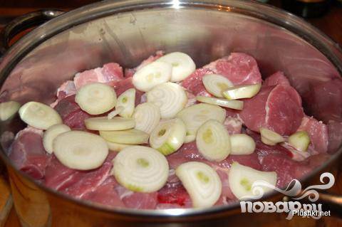 Выложить мясо в кастрюлю и покрыть луком.