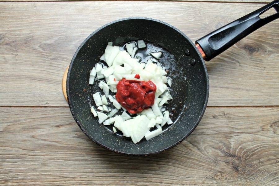 В сковороду после обжаривания ребрышек выложите нарезанный репчатый лук и томатную пасту.