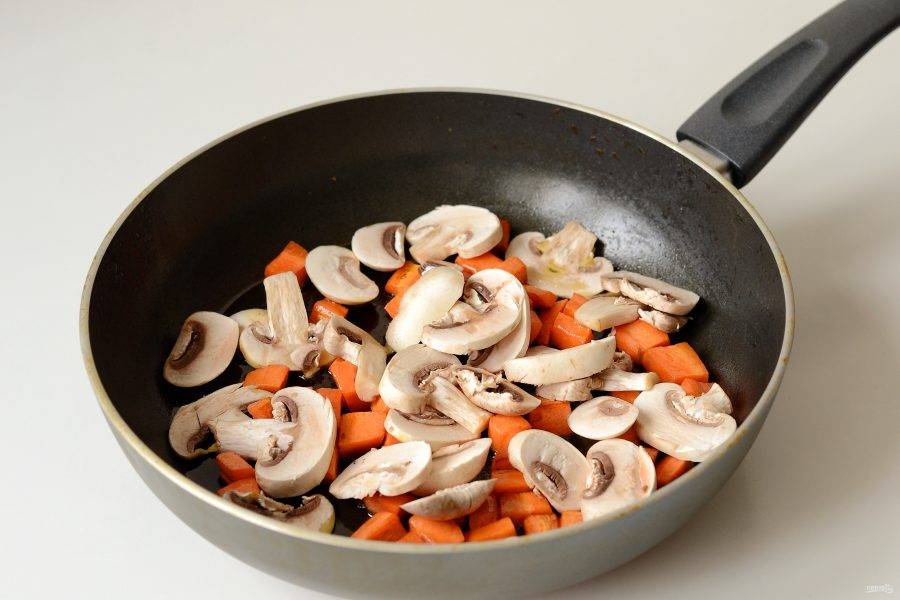 Разогрейте масло в сковороде. Добавьте морковь порезанную крупными кубиками. Обжарьте 1-2 минуты, затем добавьте шампиньоны ломтиками. Перемешайте, продолжайте жарить на среднем огне.
