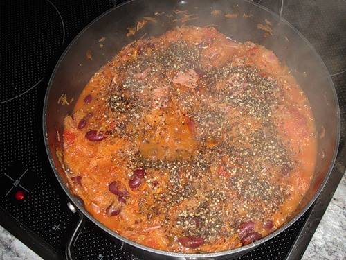 По истечении времени выкладываем к овощам нарезанные копчености и фасоль (без жидкости), добавляем томатную пасту, солим все и приправляем специями по вкусу. Тушим бигус еще минут 15-20, затем снимаем кастрюльку с огня.