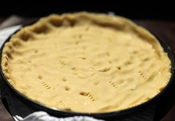 Замешиваем тесто, формируем из него шар и кладем в холодильник на 30 минут. Через пол часа раскатываем тесто и выкладываем в смазанную маслом форму, сформировав бортики. Проткните тесто вилкой в нескольких местах.