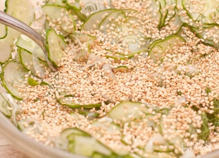 2.	Выложите огурцы в миску, добавьте тонко нарезанный полукольцами лук, поджаренные семена кунжута, 0,5-3/4 чайных ложки соли и уксус.