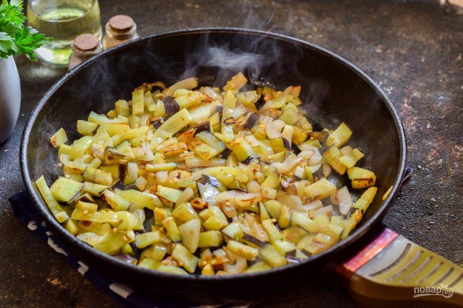 В сковороде прогрейте растительное масло, выложите лук, перец и баклажаны. Жарьте 3-4 минуты на небольшом огне.