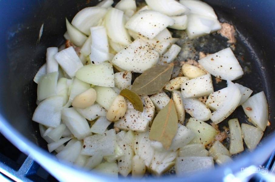6.	Выложите луковицу и целые очищенные зубчики чеснока, посолите и поперчите, добавьте лавровый лист. Обжаривайте овощи несколько минут.