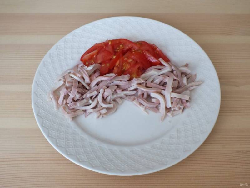 Возьмите блюдо или тарелку. Выложите противоположными секторами кальмары, между ними нарезанные соломкой помидоры черри.